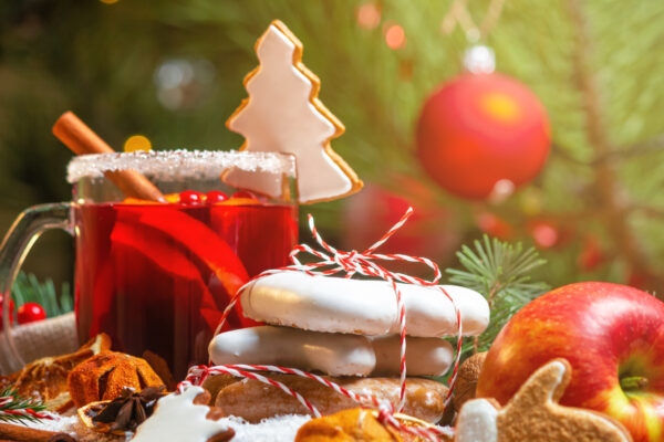 Christmas celebration concept with cup of mulled wine, Christmas cookies, fruit and spices, close up with selective focus on the background of the Christmas tree