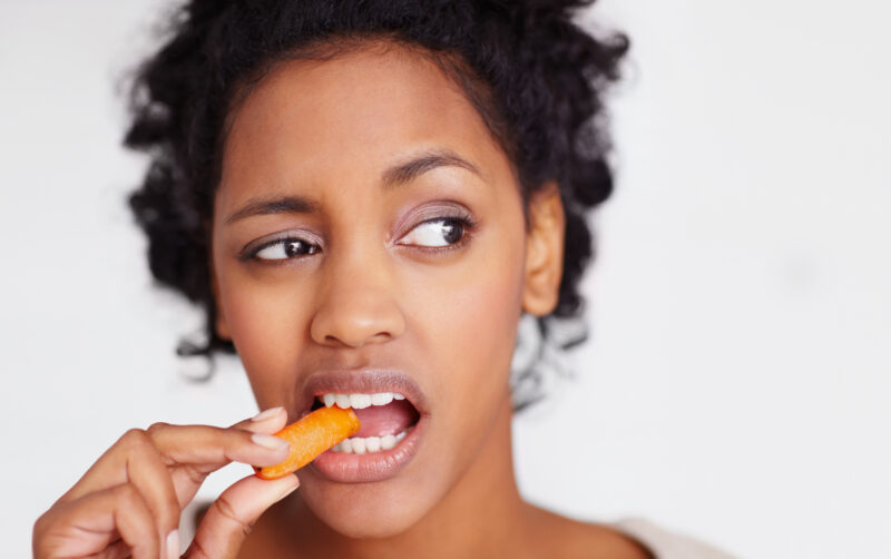 Unhappy woman eating a carrot Frau isst Karotte
